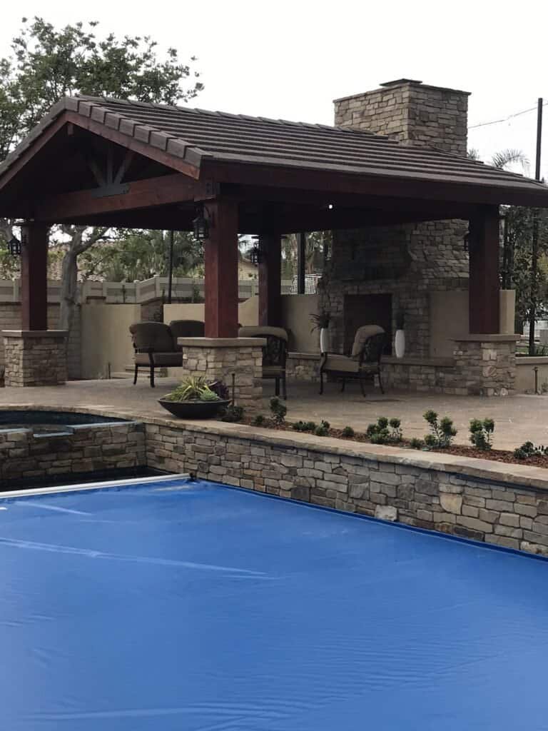Outdoor poolside pavilion with fireplace and seating area for relaxation.