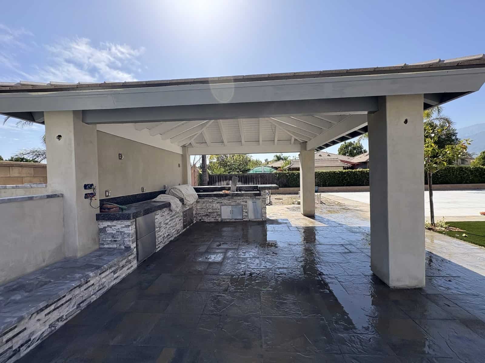 Modern outdoor kitchen with built-in grill and seating area under a covered patio.