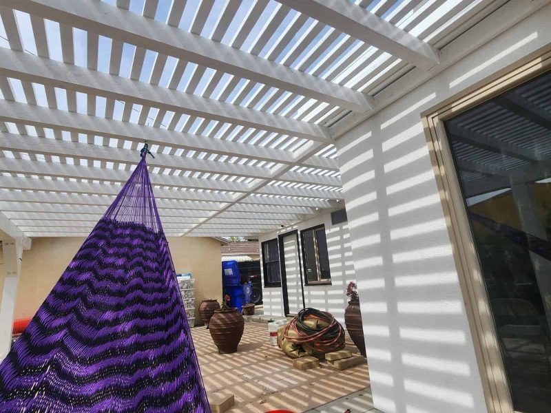 Outdoor patio with white pergola casting striped shadows and a purple hanging hammock.