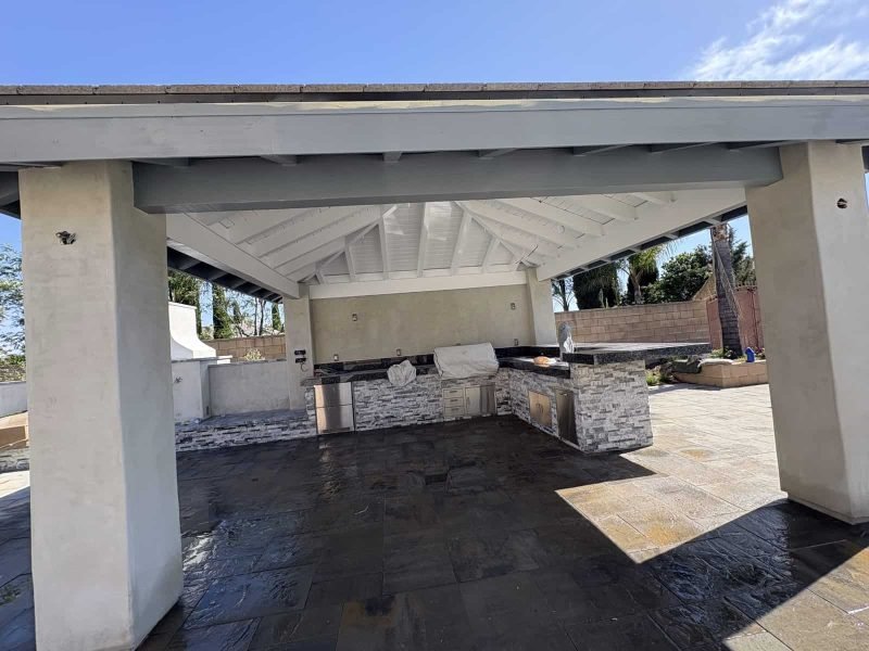 Modern outdoor kitchen with stone countertops and a white gabled roof.